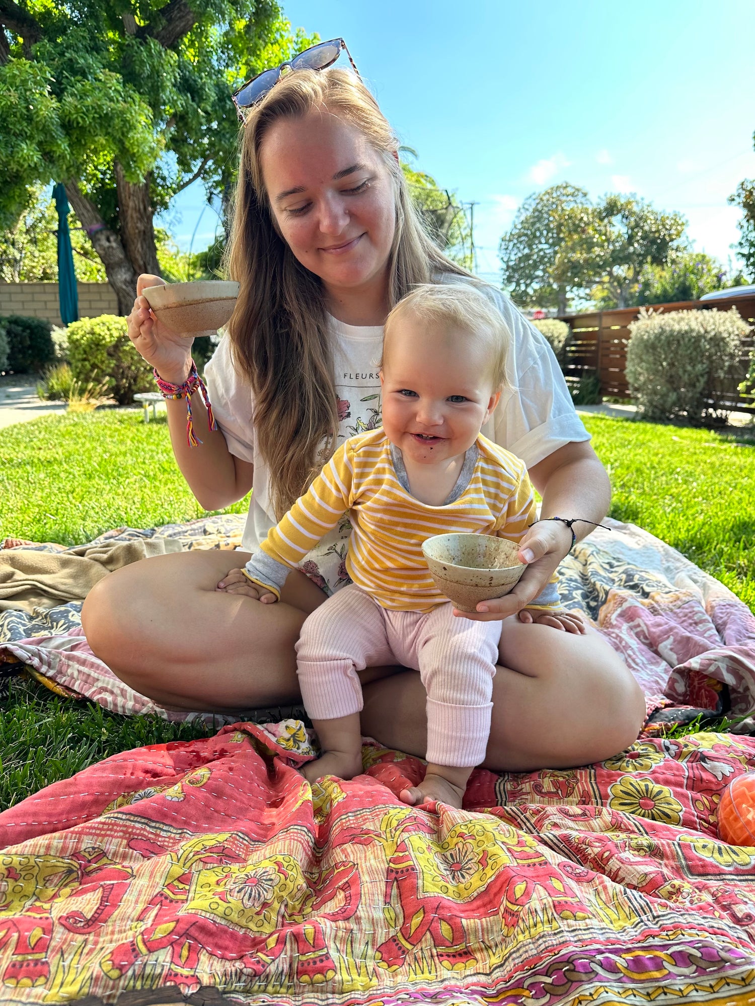 Audrey, the founder of the Mindful Milling Co. sitting with her youngest daughter on a blanket in the grass during a tea ceremony.